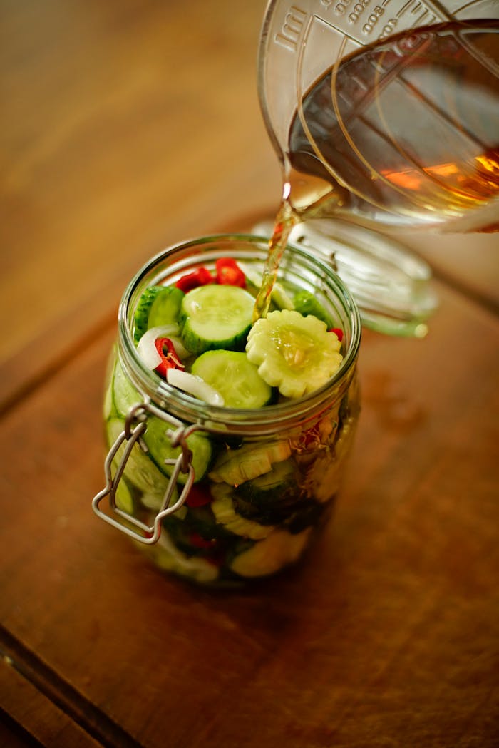 Close-up of pouring liquid into a jar of fresh cucumber slices, ideal for food blogs.