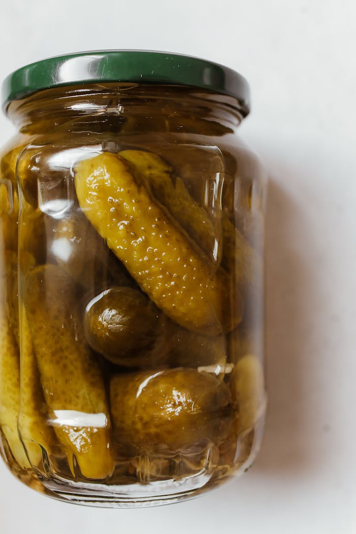 A close-up view of a sealed jar containing pickled cucumbers on a plain background.