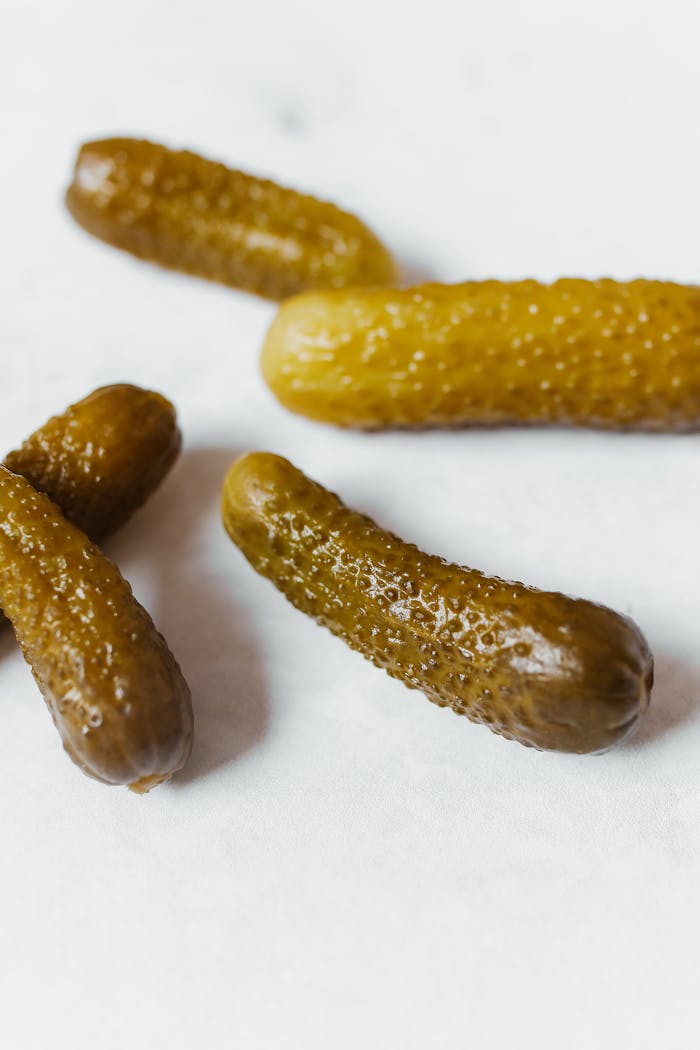 Five pickled cucumbers on a white surface, showcasing texture and color.