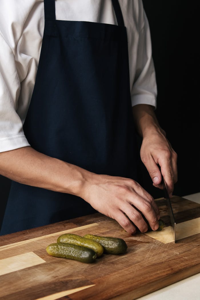 A chef expertly cuts pickles on a wooden board. Ideal for culinary themes.