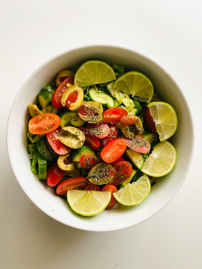 Colorful salad with lime, cherry tomatoes, and olives in a white bowl.