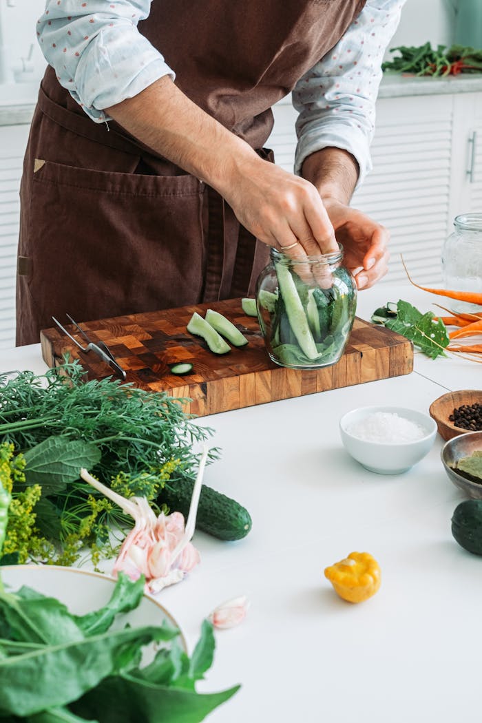 A man preparing pickled cucumbers with fresh ingredients on a kitchen counter.
